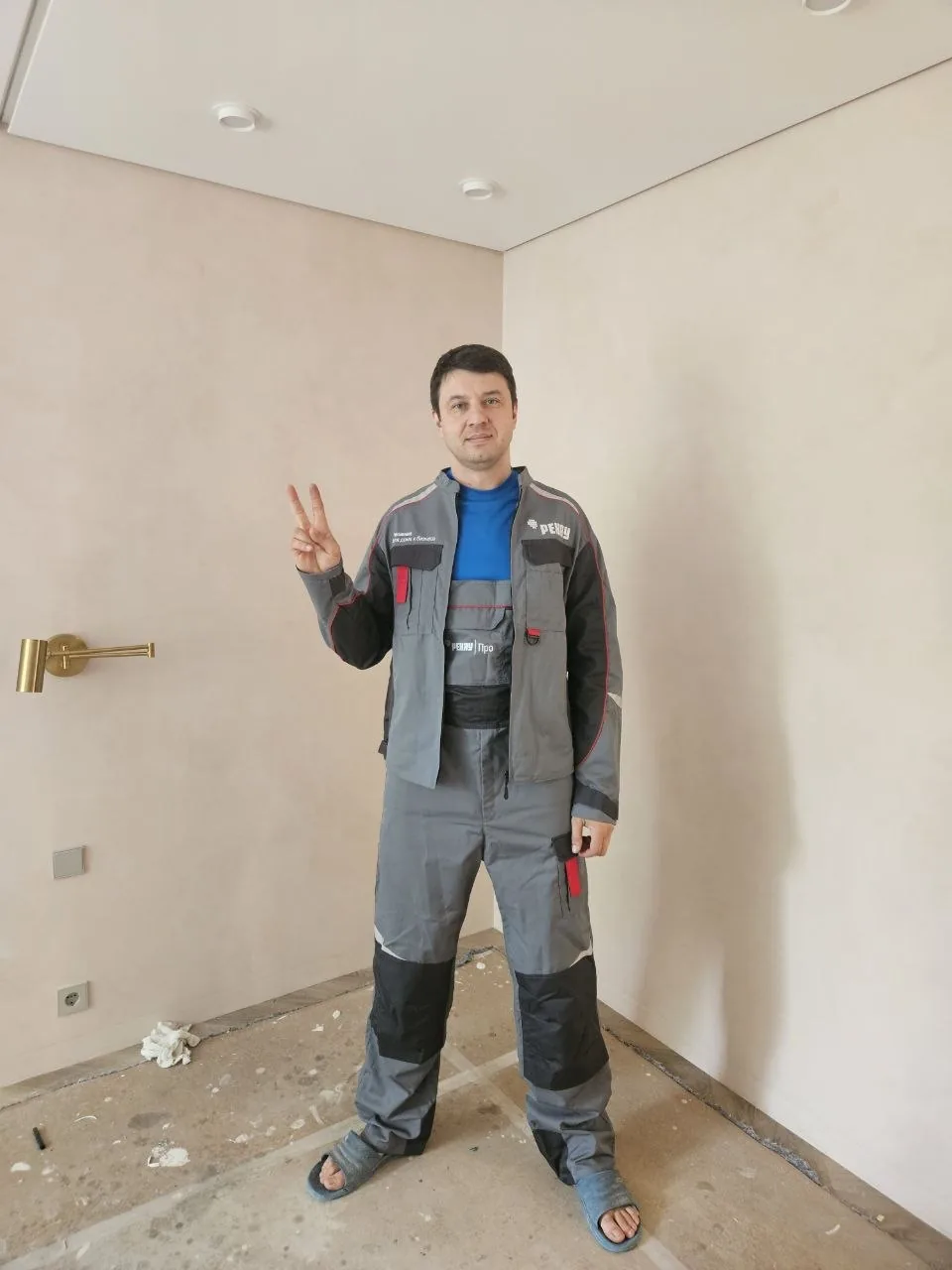 Рабочий в отделанном светлом помещении показывает жест победы