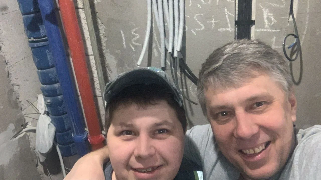 Двое рабочих фотографируются в техническом помещении с трубами